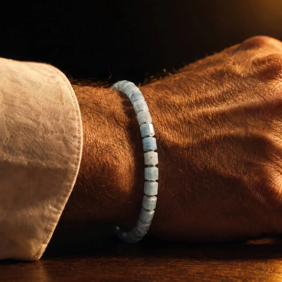 Aurum Brothers Aquamarine Bracelet XXVI with pale blue 6mm beads, worn beside a cream shirt cuff in warm light.