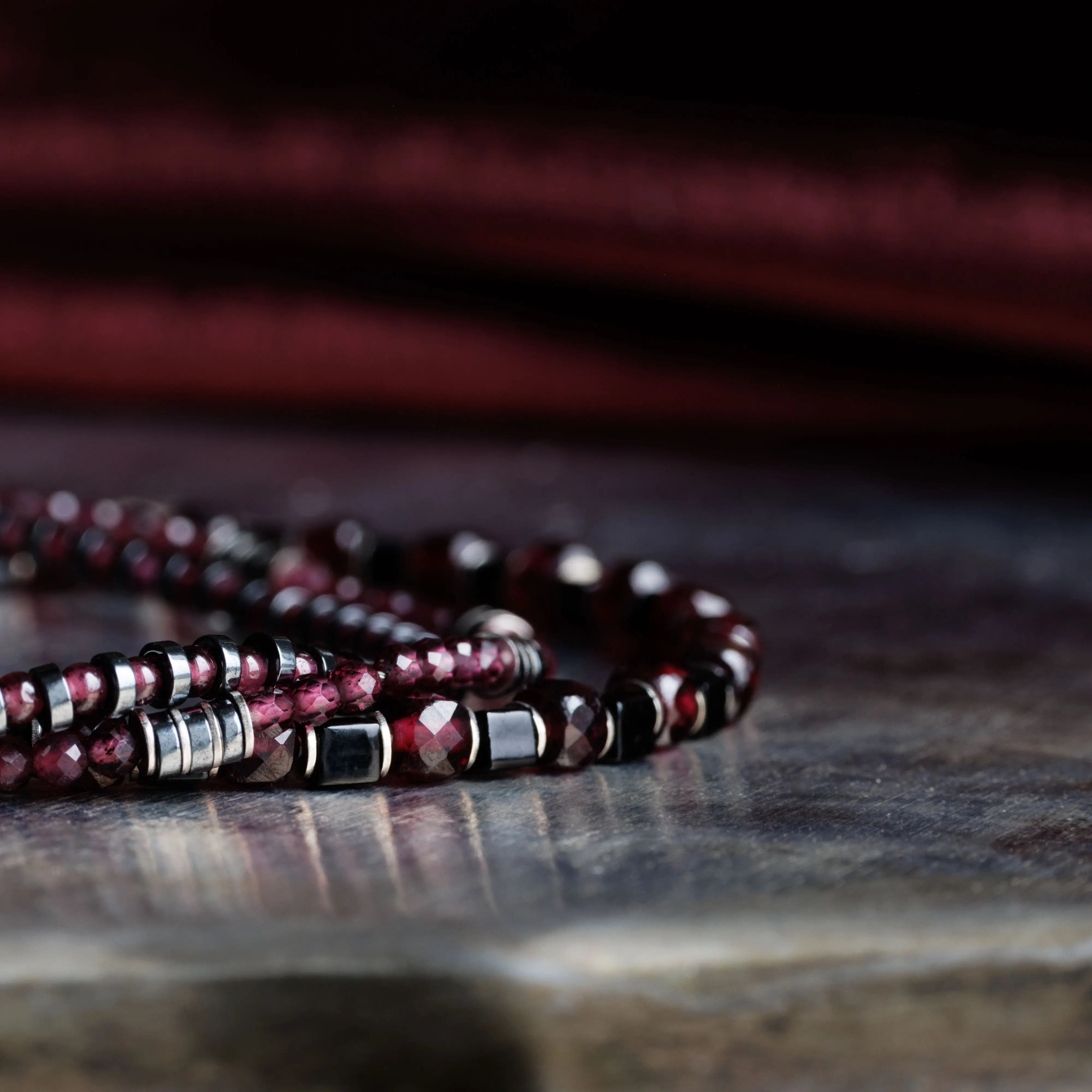 Close-up of Red Garnet Bracelet XIII showcasing 2mm garnet stones, hematite accents, and intricate craftsmanship on a metallic surface.