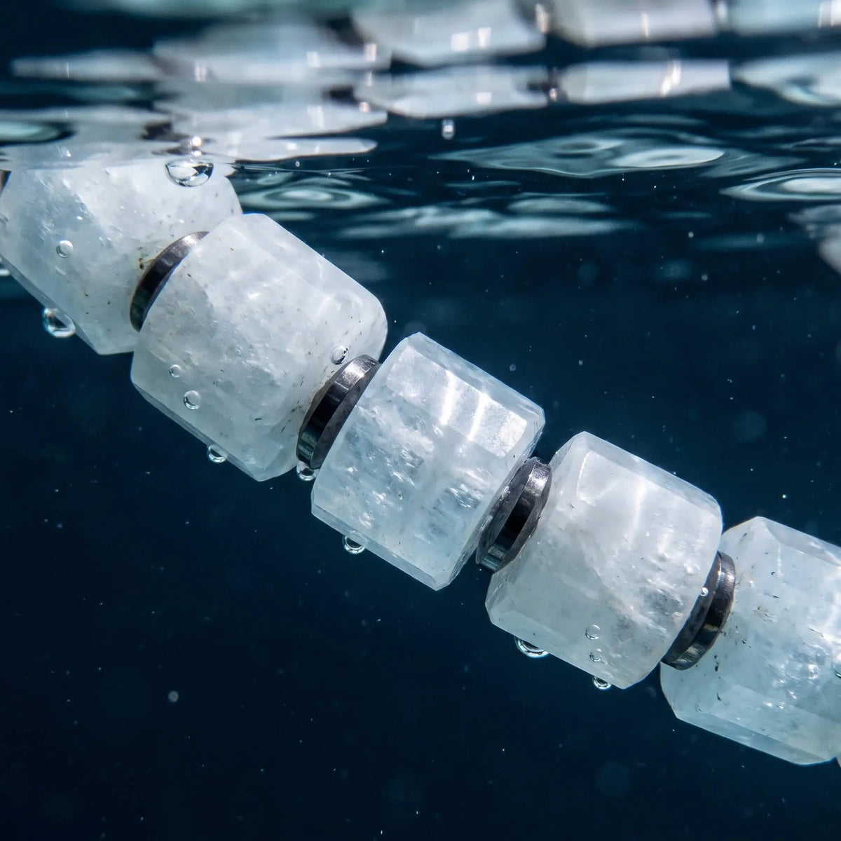 Close-up of pale blue aquamarine beads and hematite spacers on the Aquamarine Bracelet XXVI, photographed beneath the water's surface.